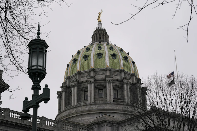 A domed building topped with a gold figure. Flags fly at half staff on pole near the dome.