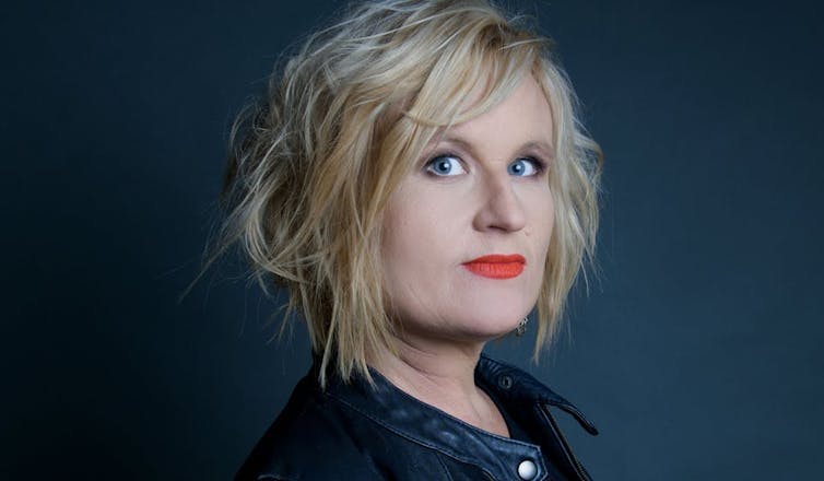 a blonde woman with red lipstick and tousled hair, in a leather jacket