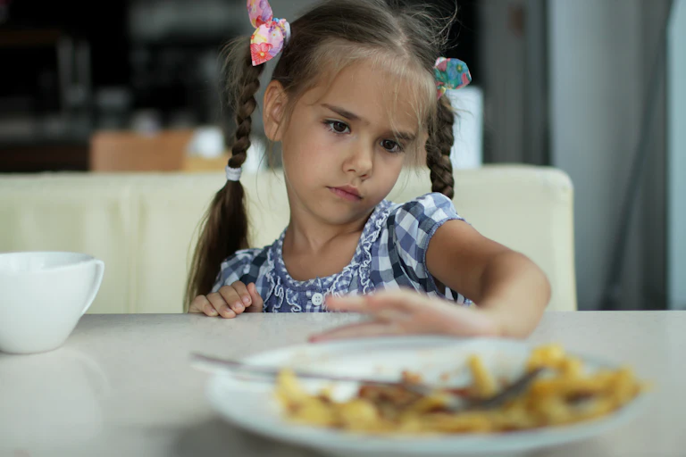 A young girl pushes her plate away