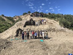 A group of people standing on a bare slope that shows signs of excavation