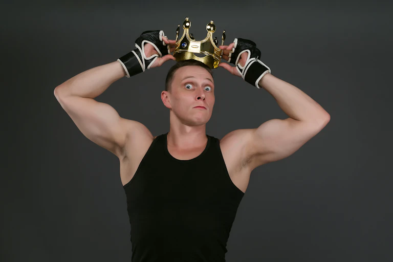 un homme jeune avec un marcel noir musclé il se met une couronne sur la tête. son visage montre qu'il n'est pas dupe.