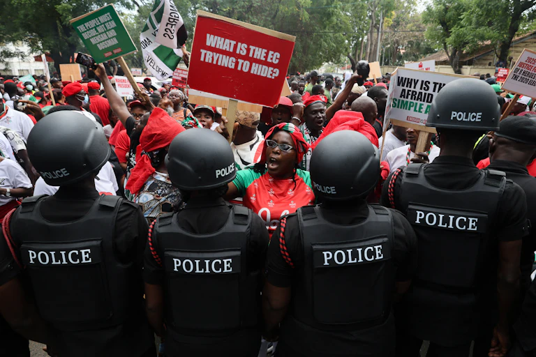 People on a street, holding up posters, facing a line of police in uniform