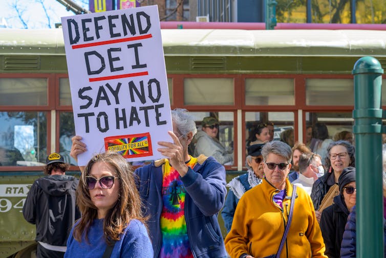 prostesters in los angeles holding a placard that reads 'defend dei say no to hate'