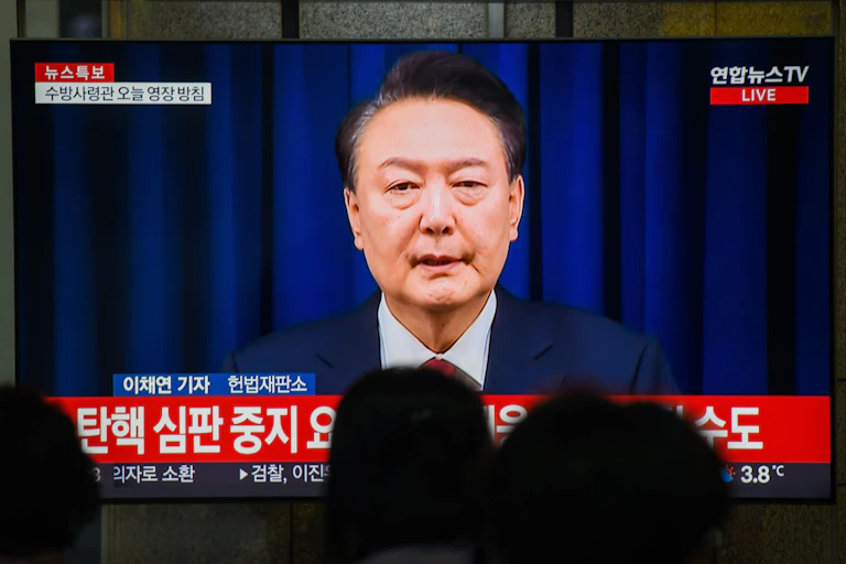 A Korean man in a suit addressing people directly on television.