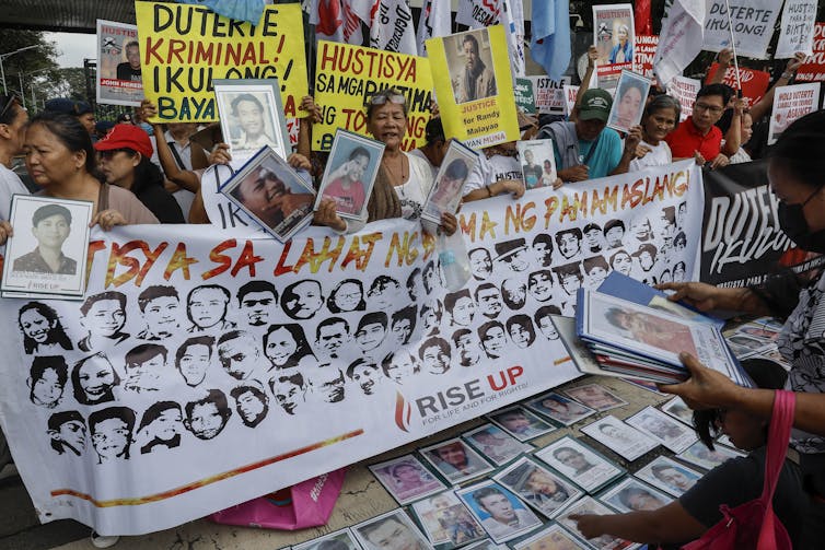 Opponents of former Philippines president Rodrigo Duterte demonstrate with a banner showing victims of the war on drugs and calling for his arrest.