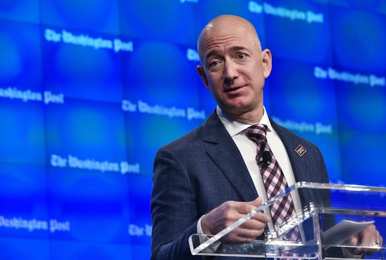 A bald man in a jacket and tie standing at a lectern.
