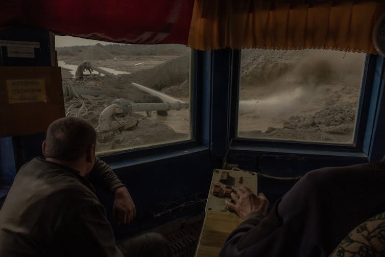 Two people look out windows at equipment operating in a mine.