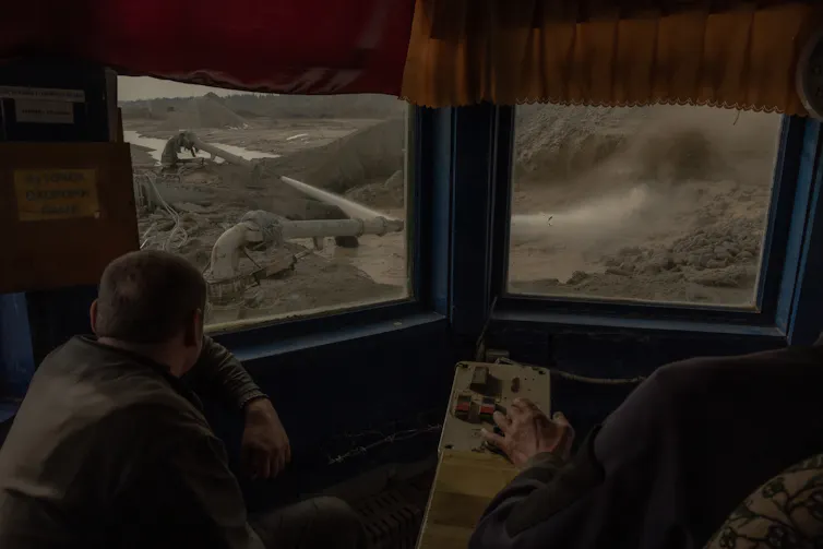 Two people look out windows at equipment operating in a mine.