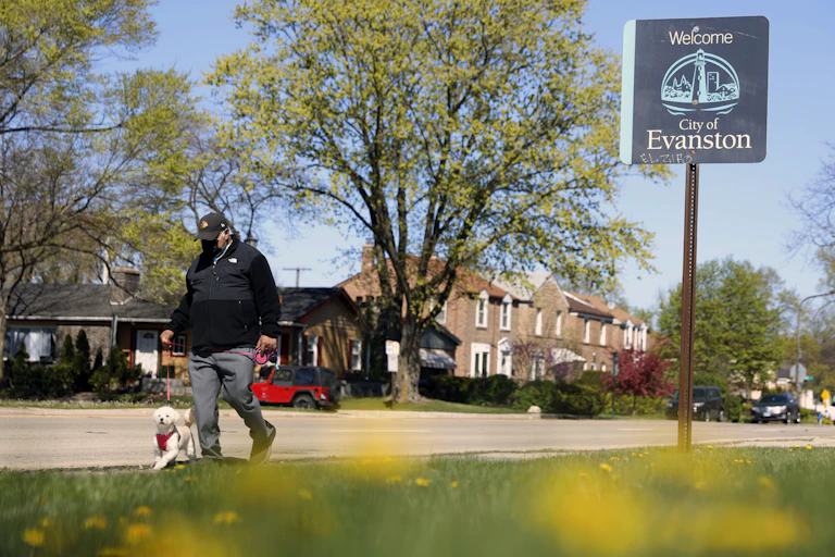 A man walks a dog near a sign that reads, 'Welcome to City of Evanston'