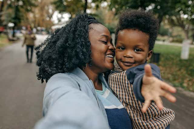 A smiling mother holds her young son while strolling in the park.