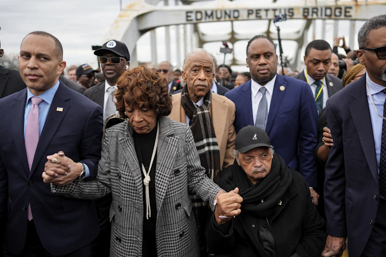 Prominent civil rights leaders walk across the Pettus Bridge holding hands. Jackson is in a wheelchair.