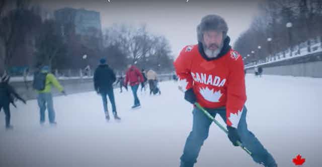 A man in fur hat with a Canada hockey sweater and a hockey stick skating.