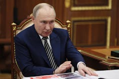 A pale balding man sits at a desk.