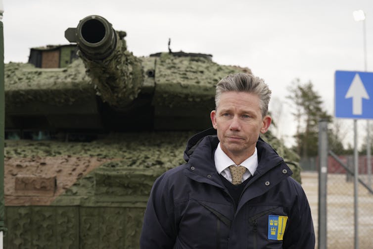 A white man with short, greying hair stands in front of a tank