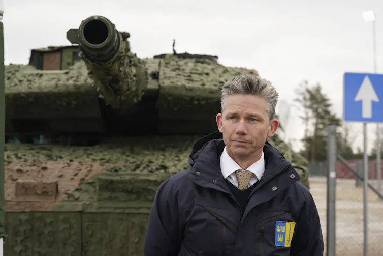 A white man with short, greying hair stands in front of a tank