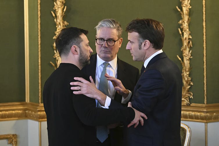 Three men, two in suits, huddle and speak.