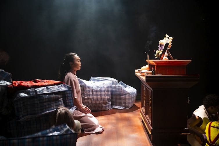 Production image: a woman kneels in front of an altar.
