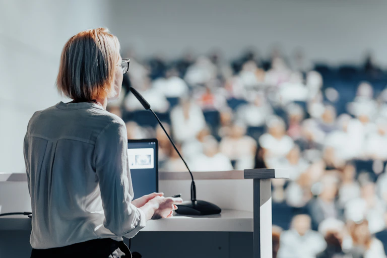 A woman stands at a lectern and speaks to an audience.