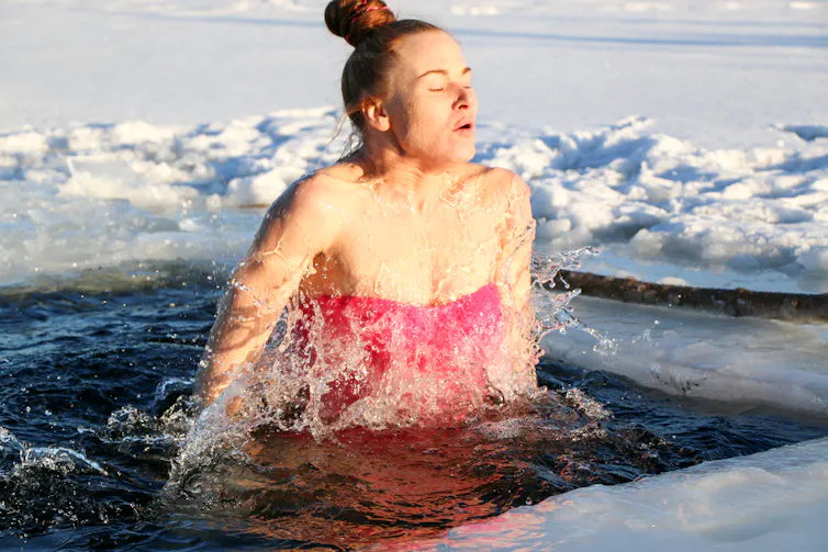 A woman emerges from water in a frozen lake.