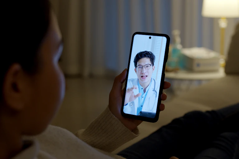 Woman sits in dark looking at a doctor speaking on her phone.
