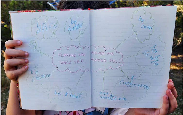 A child holds up a page of writing with their emotions about the flood.