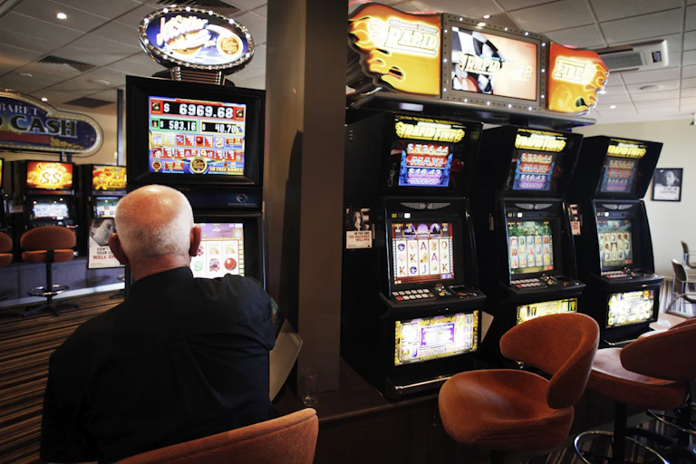 An elderly man plays a poker machine alone