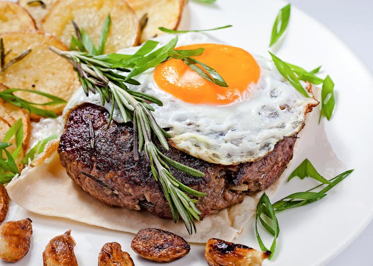 Fried egg on top of steak on plate with rosemary sprig