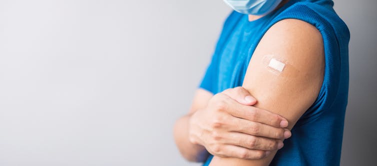Man wearing face mask showing arm with vaccine plaster