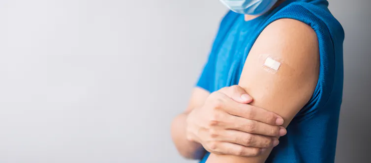 Man wearing face mask showing arm with vaccine plaster