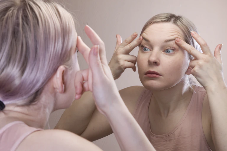 A young woman closely scrutinising her face in a mirror
