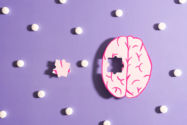 An illustration of a brain with jigsaw piece missing surrounded by pills