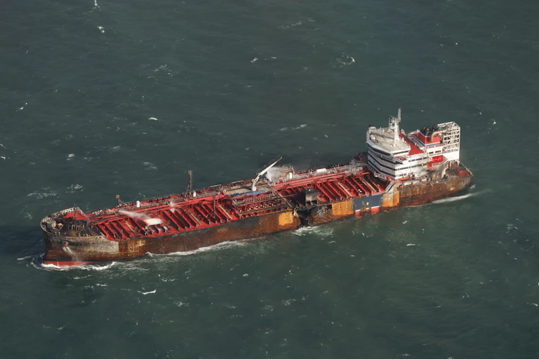 A red oil tanker at sea with a black hole in its hull.