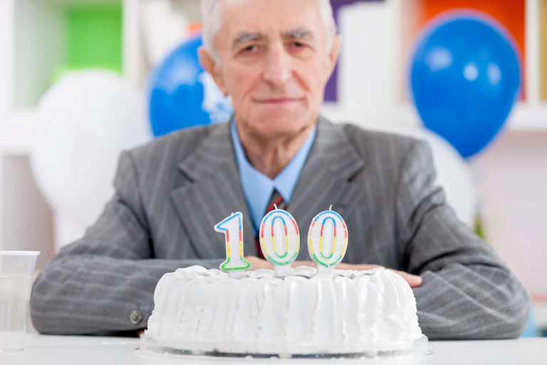 Homme âgé devant un gâteau d'anniversaire sur lequel ont été déposées des bougies 100 ans