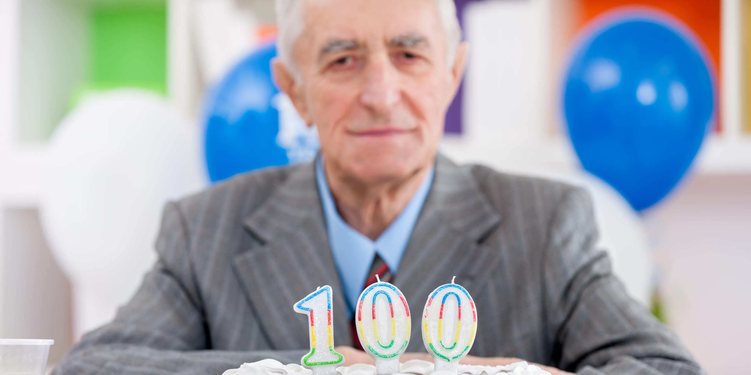 Homme âgé devant un gâteau d'anniversaire sur lequel ont été déposées des bougies 100 ans