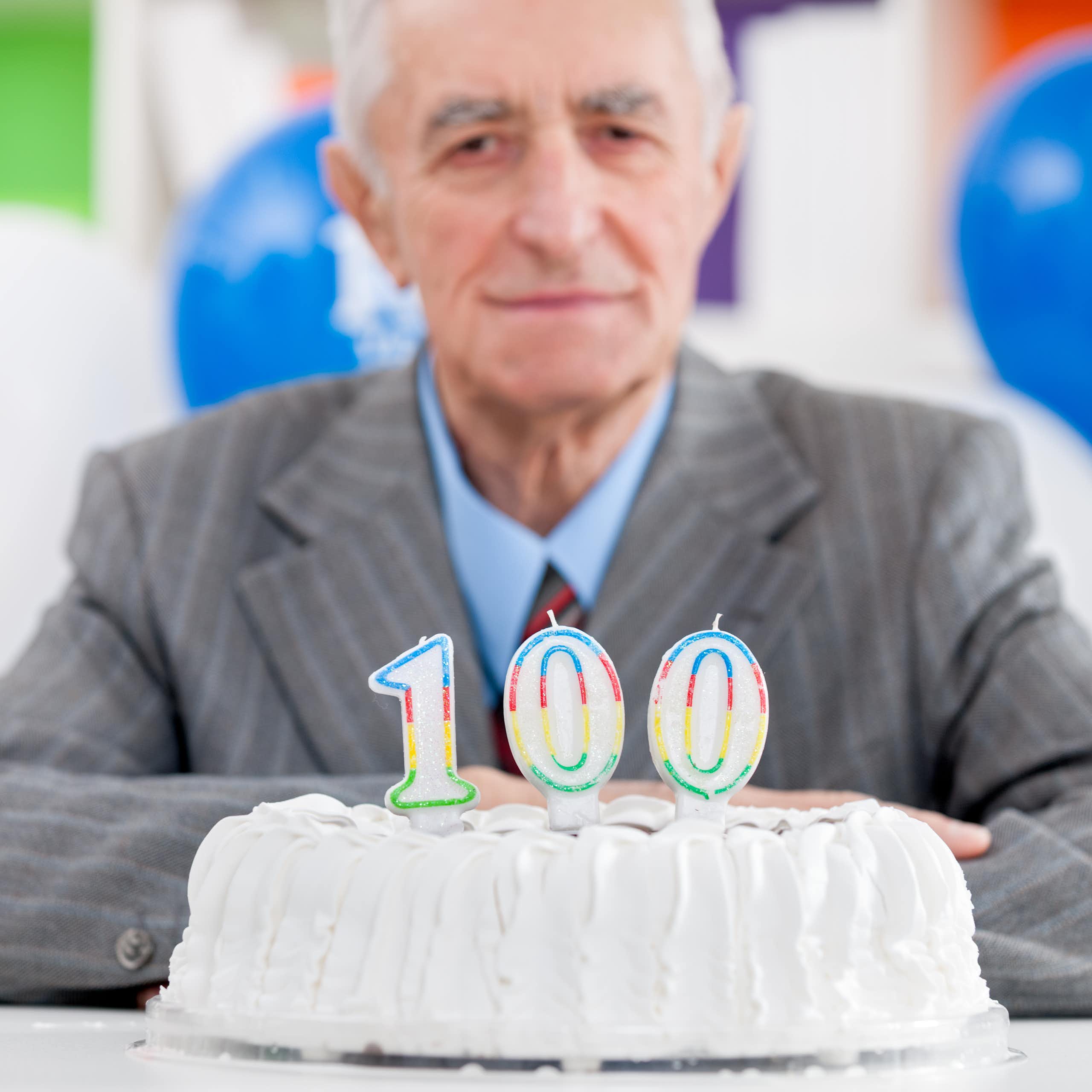 Homme âgé devant un gâteau d'anniversaire sur lequel ont été déposées des bougies 100 ans