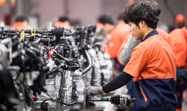 assembly plant workers in china assembling a car engine.