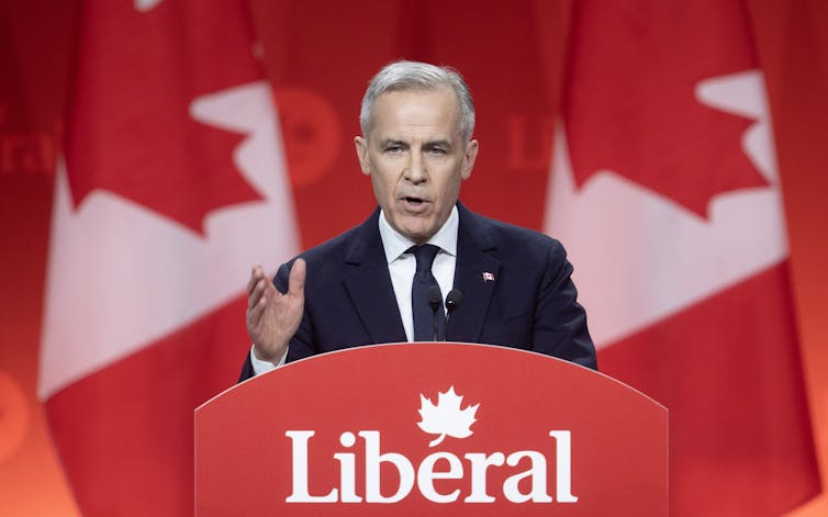 El hombre blanco con un cabello gris corto habla detrás del podio que dice liberal. Detrás de él hay dos banderas canadienses