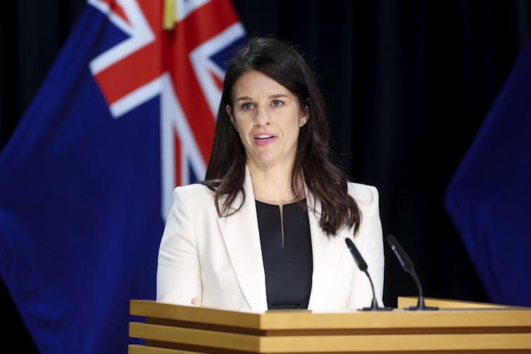 Female politician Erica Stanford standing in front of New Zealand flag in front of a podium