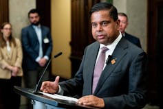 El hombre del sur de Asia en el traje habla en un micrófono detrás del podio