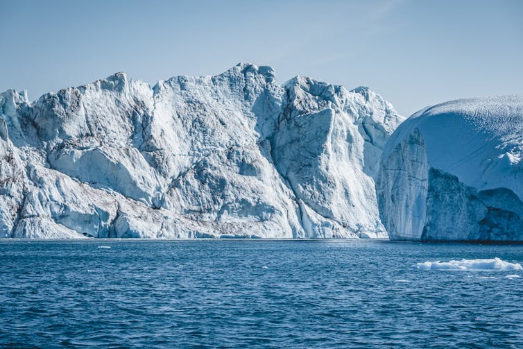 Sun shining on a large ice cliff face that drops into the ocean.