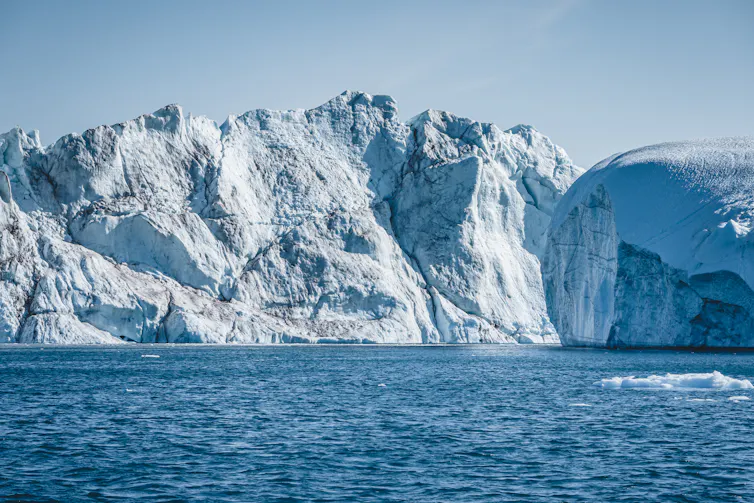Sun shining on a large ice cliff face that drops into the ocean.
