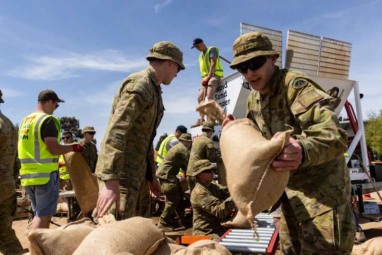Several Australian soldiers in afrmy fatigues filling and carrying sand bags