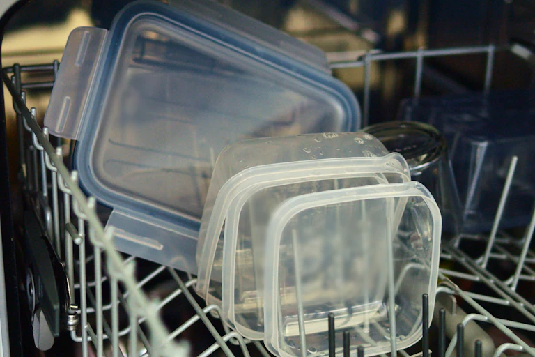 Plastic containers stacked in the top drawer of a dishwasher.