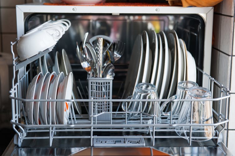 Front view of a small dishwasher full of cutlery, cups and plates.
