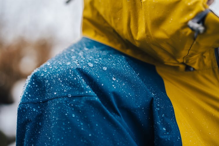 Close-up of a man's shoulder with water beading on a yellow and blue rain jacket.