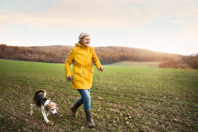 A woman walking with a dog in a field.