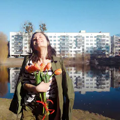Picture of a woman holding flowers and lifter her head to the sky with eyes closed.