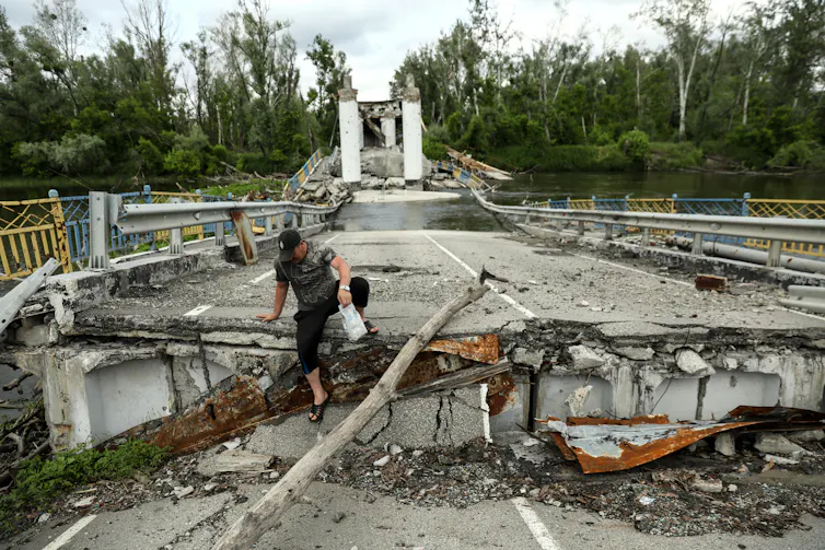 A man sits on the edge of a destroyed bridge.