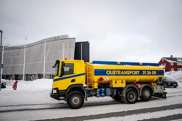 A yellow truck with an oil tank on the bank in a snowy street.