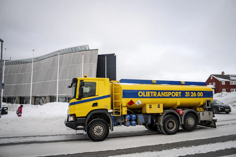 A yellow truck with an oil tank on the bank in a snowy street.